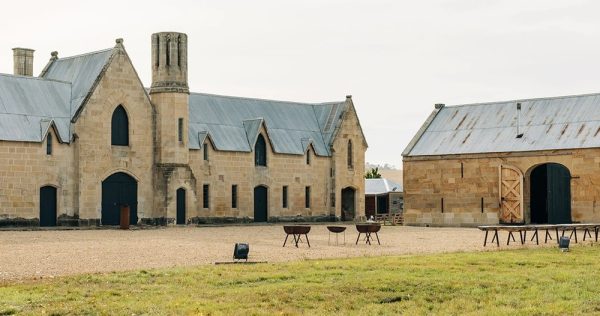 an old sandstone building with dark tin roof - the home of Lark Distillery Pontville Tasmania. Firepits are on the gravel courtyard foreground